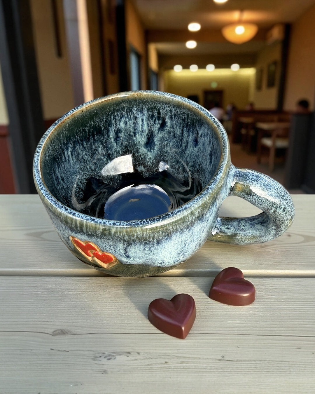 Blue glazed stoneware mug with hearts, handmade ceramic, deep blue glaze, red hearts detail, perfect for coffee or tea.