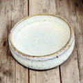 Handmade ceramic cat bowl with natural tones, shallow shape, and soft glaze on a wooden background.