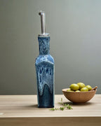 Handmade Ceramic Olive Oil Bottle in deep blue glaze with stainless steel pourer, accompanied by a bowl of green olives.