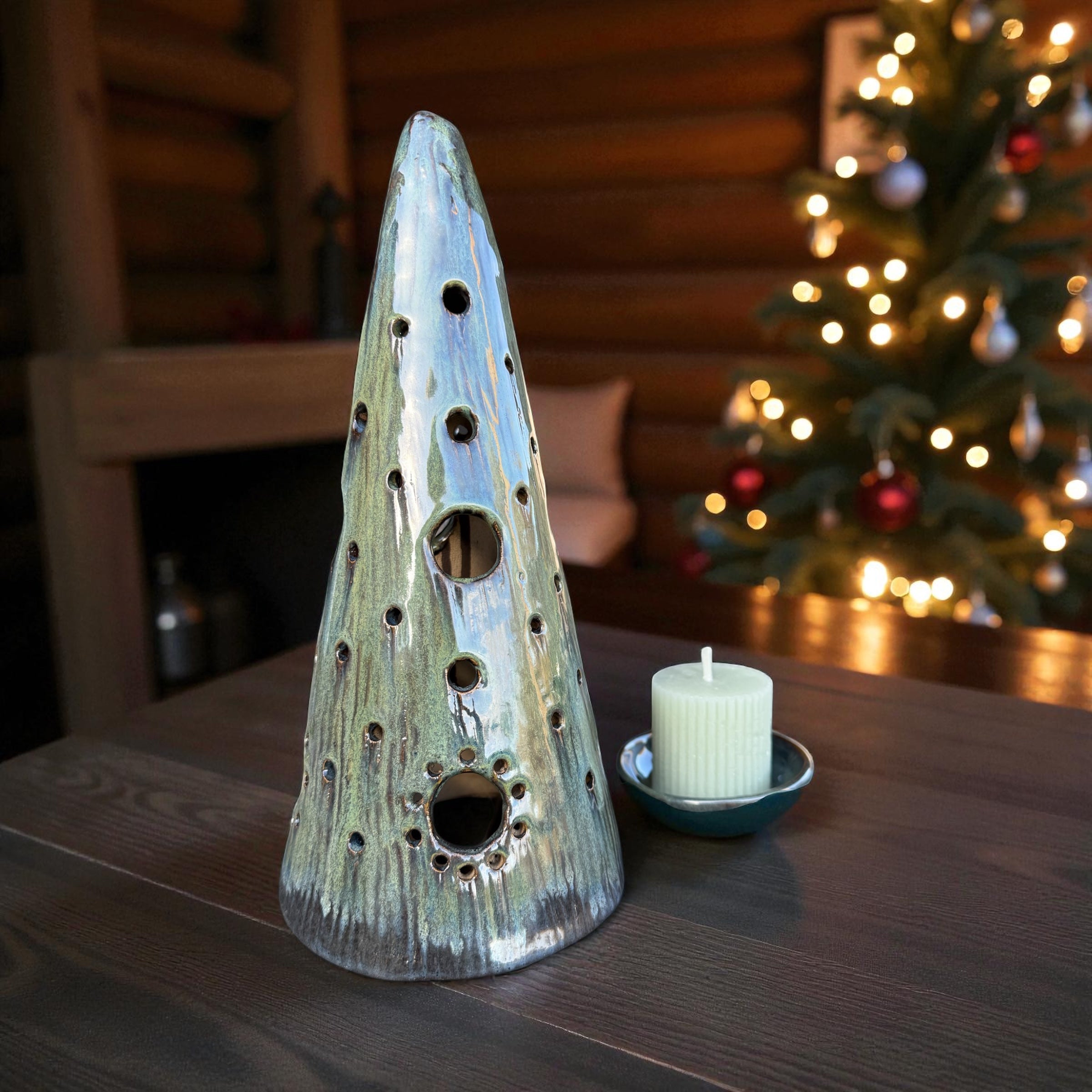 Handmade ceramic tealight tree in forest green glaze with candle on table, casting soft light patterns.