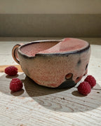 Ceramic berry rinsing mug with soft strawberry glaze beside fresh raspberries on a wooden table.